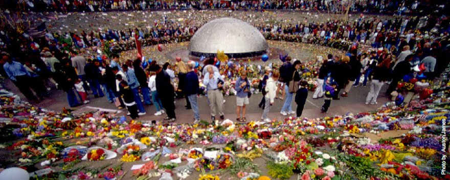 People gathered around the International Fountain at Seattle Center. The fountain is turned off. There are many flowers that have been laid around the fountain walls.