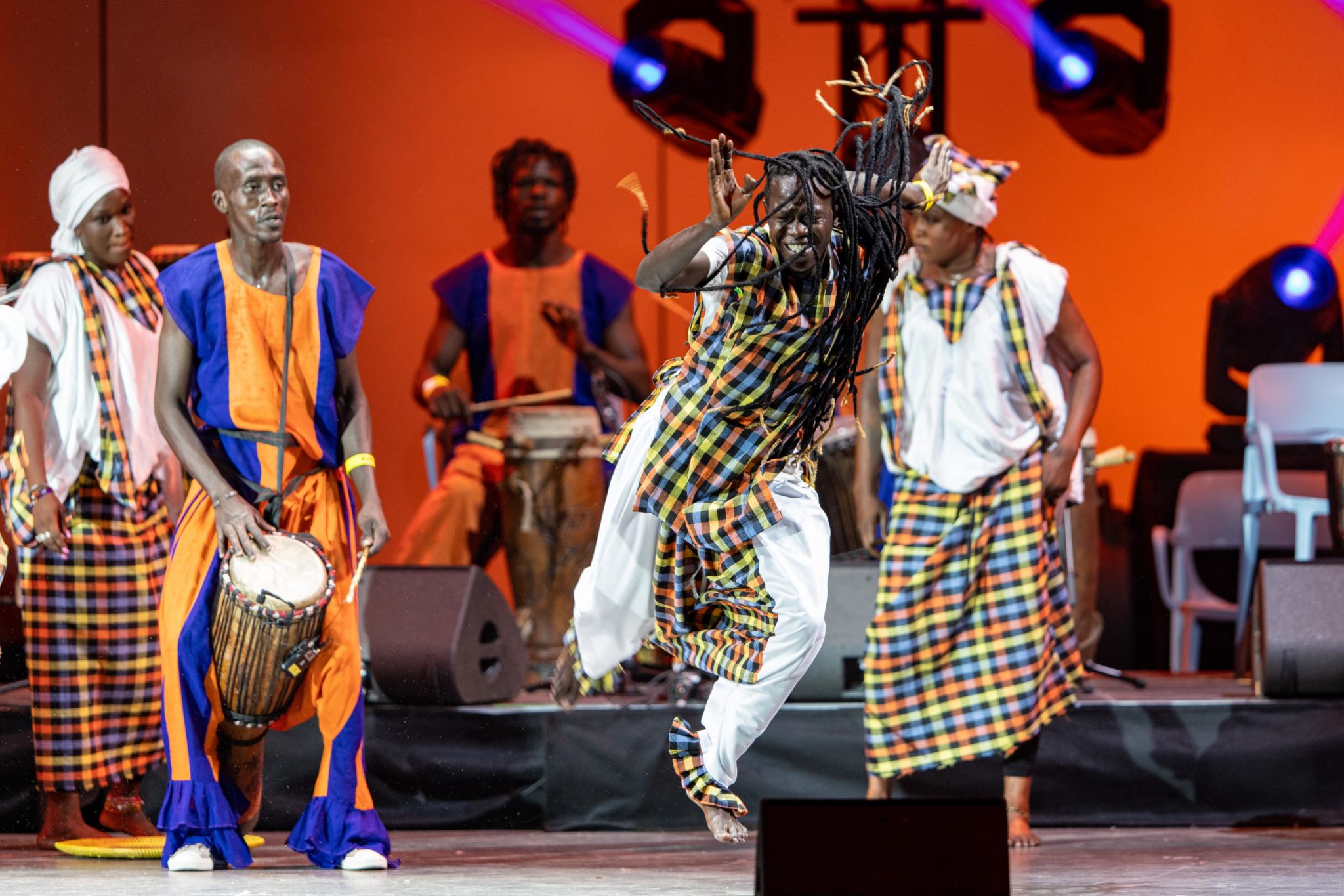 Dance performers, drums, chairs, stage, men and women wearing colorful checkered clothing