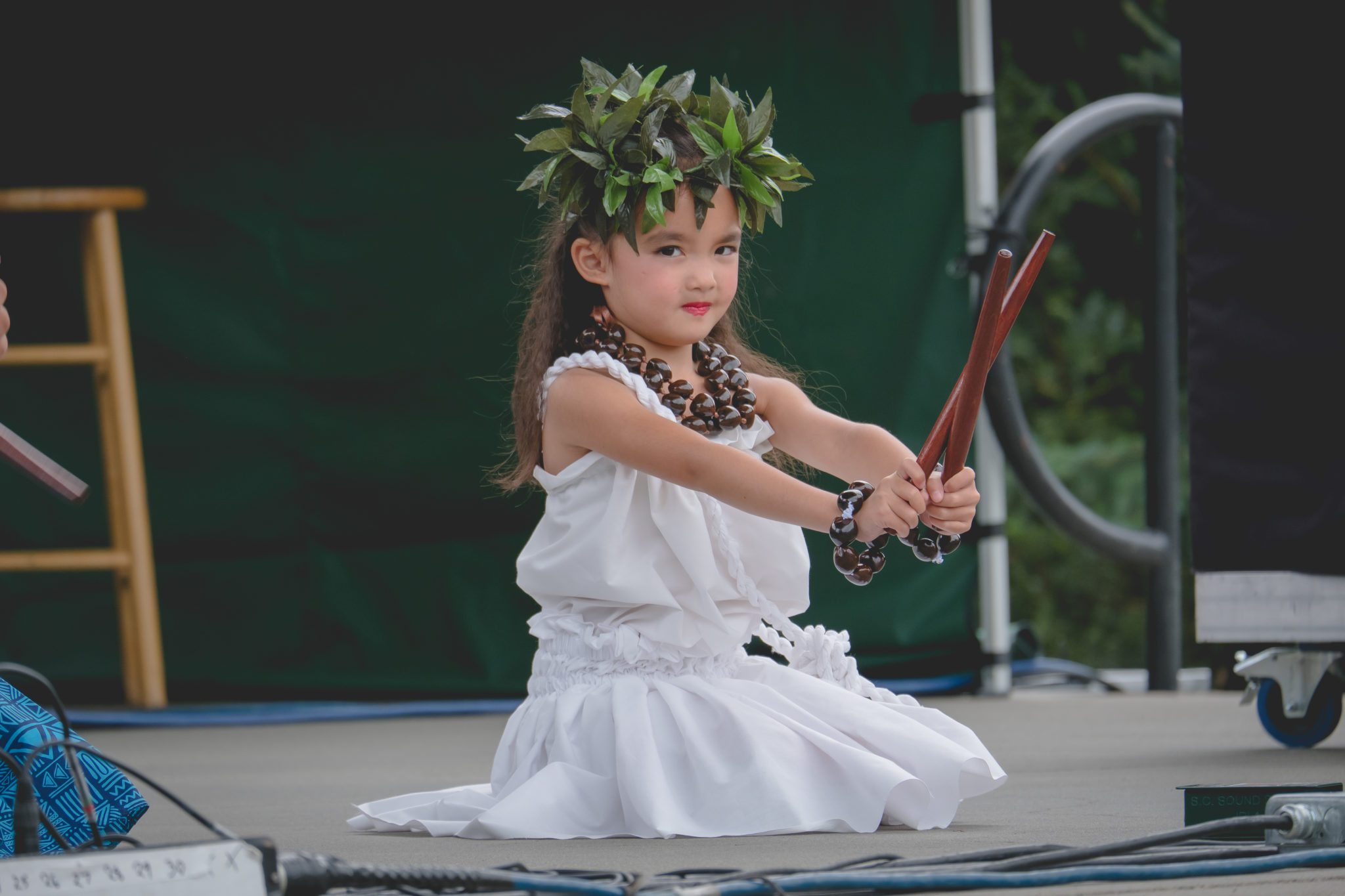 Young girl performer sitting on a stage holding sticks.