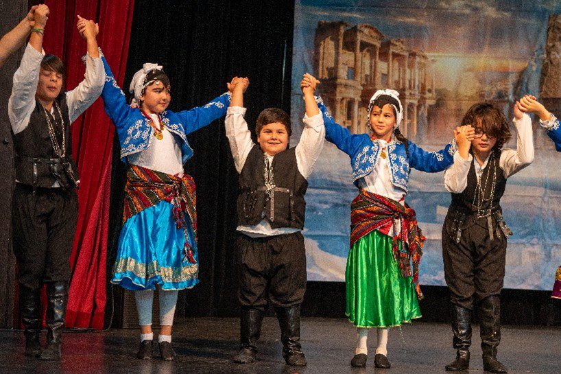 Children holding hands with arms raised standing on a stage.