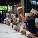 A group of kids at a table learning to spin pizza dough